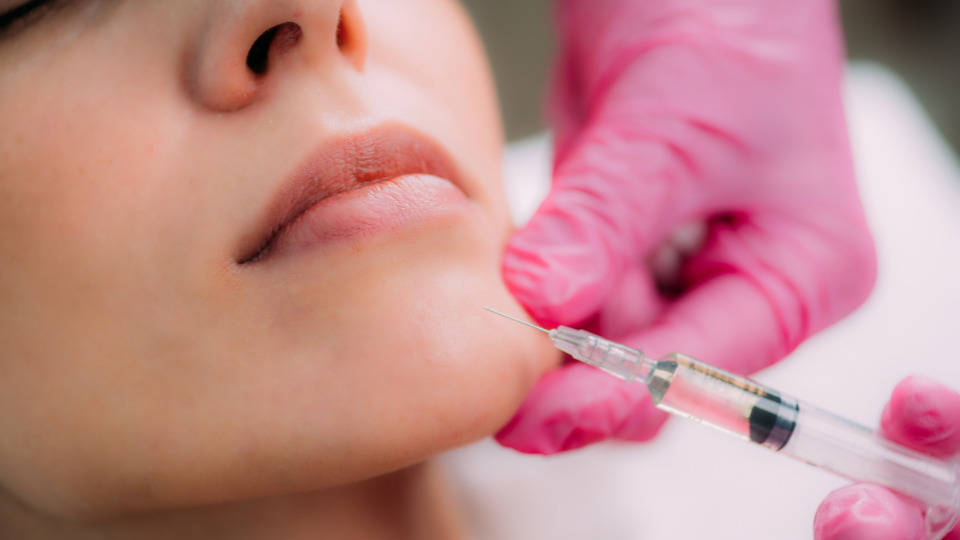 Close-up of a chin contouring procedure with a syringe and pink-gloved clinician, featuring BOTOX and Juvederm/Restylane treatments for facial contouring