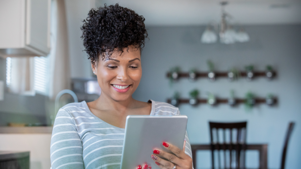 Woman with curly hair smiling while using a tablet in a home setting.