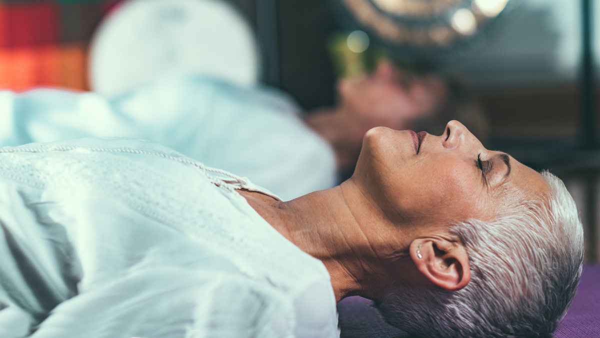 Two individuals lying down with eyes closed, engaged in guided meditation during a wellness session.